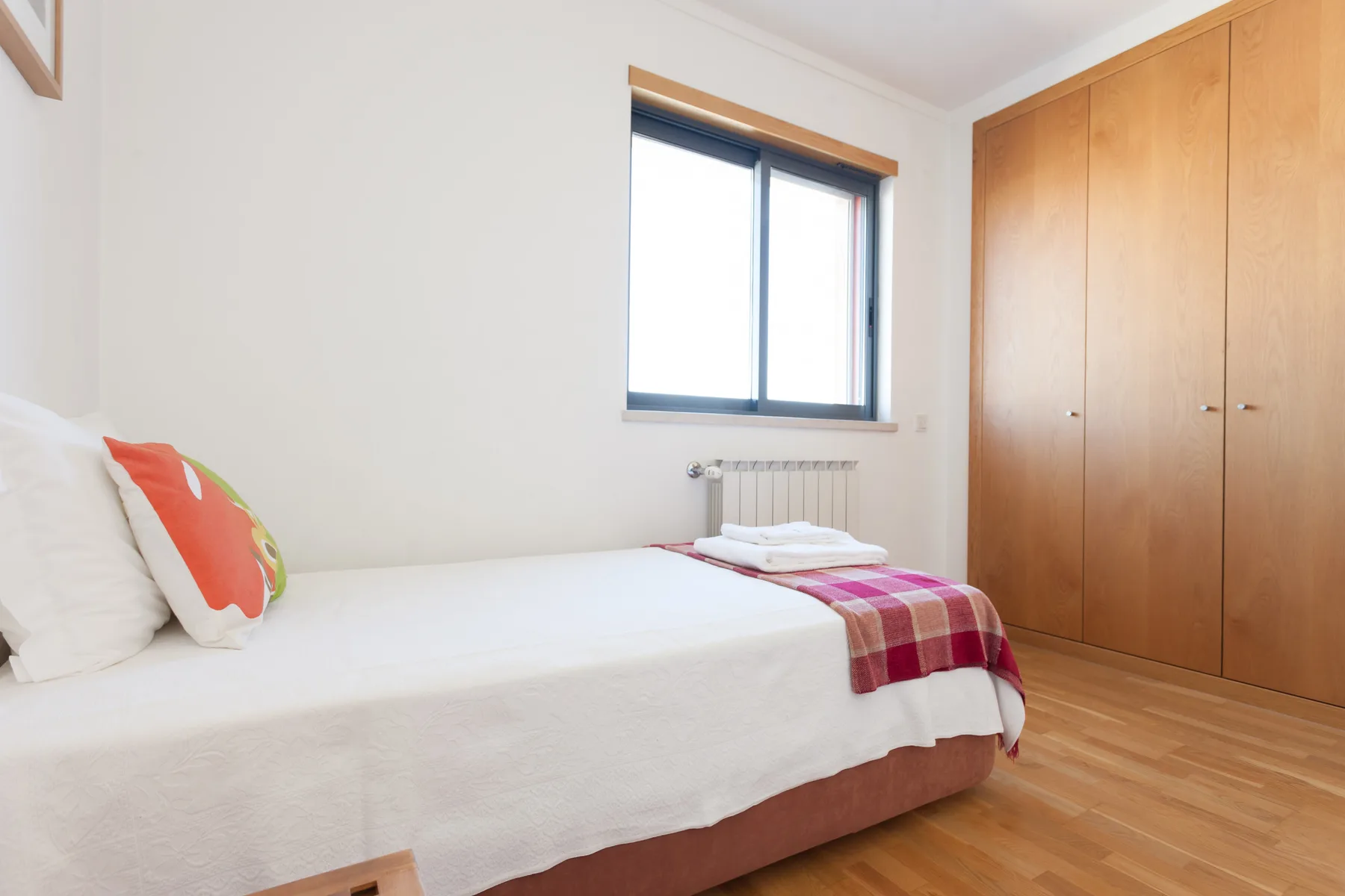 A bedroom with a bed, a window, and a wooden wardrobe.