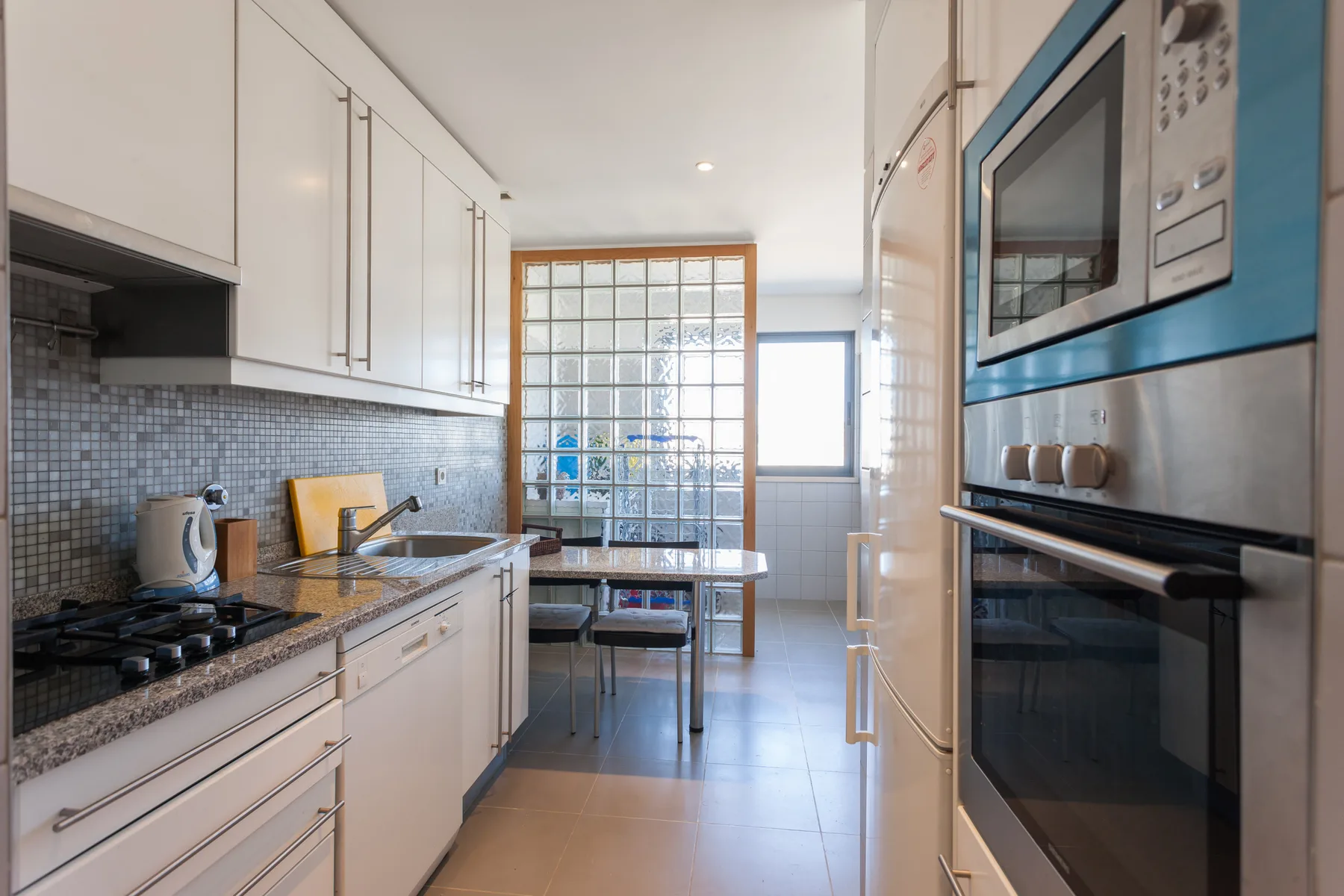 A bright kitchen with white cabinets, a tiled backsplash, and a dining table.