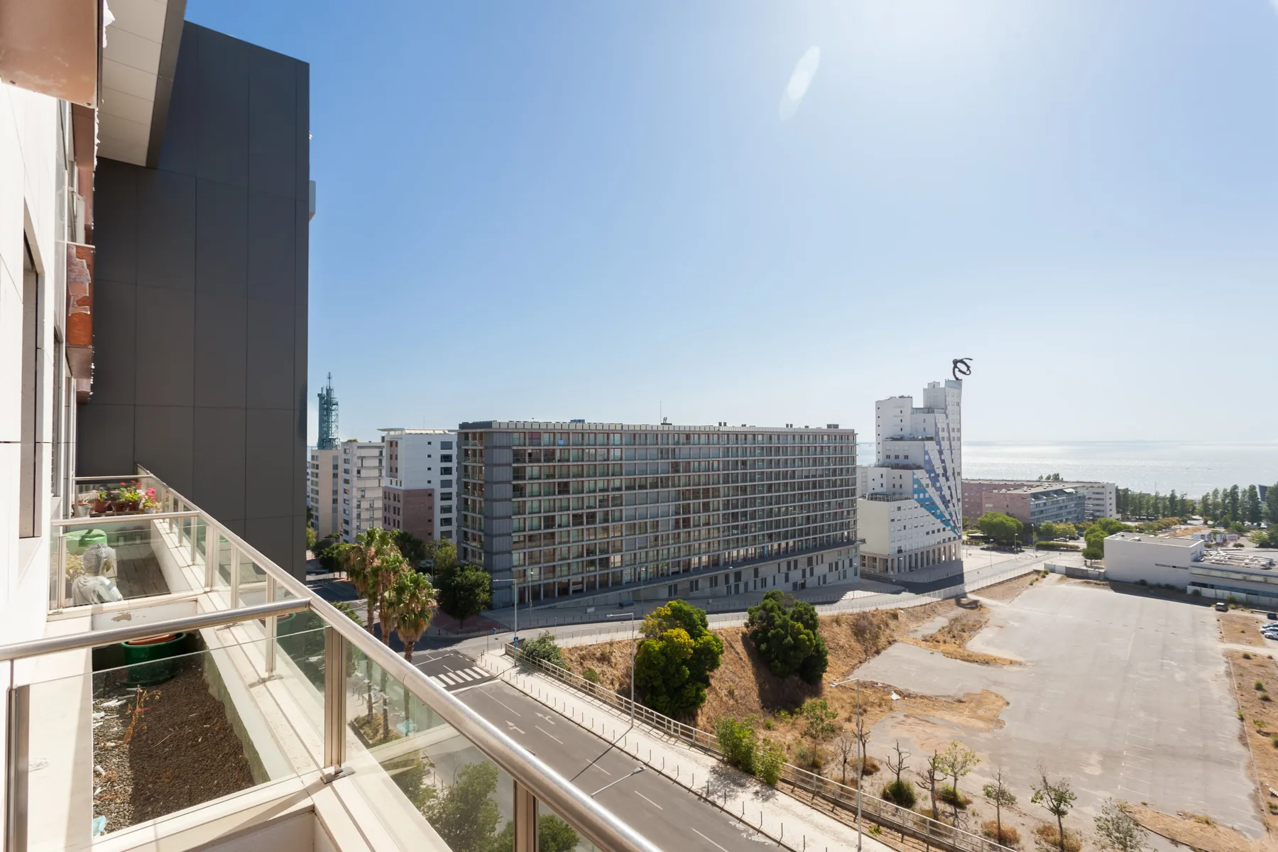 A balcony overlooks modern buildings, a roadway, and the waterfront.