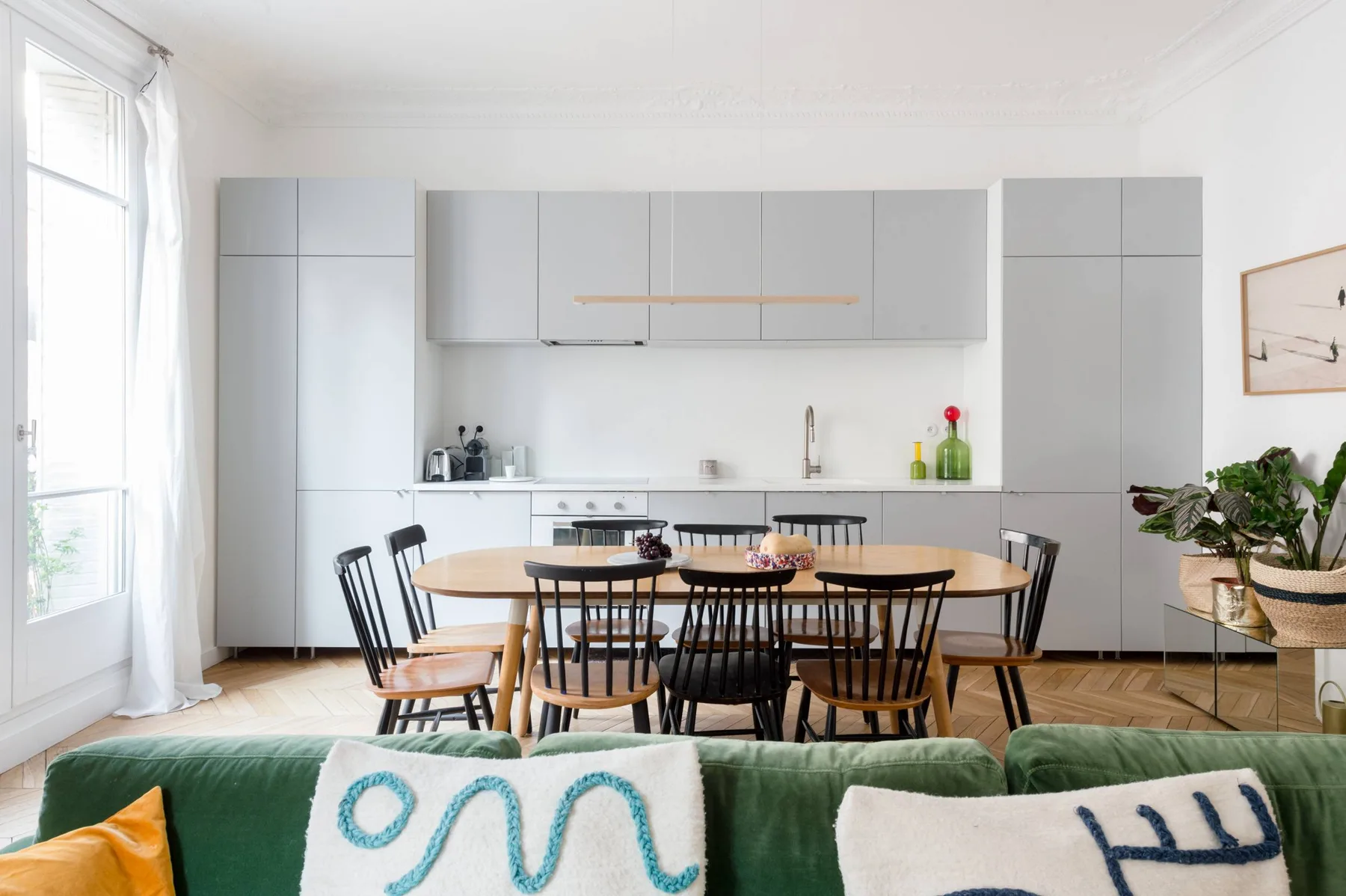 A bright dining area with a wooden table in front of a modern kitchen.