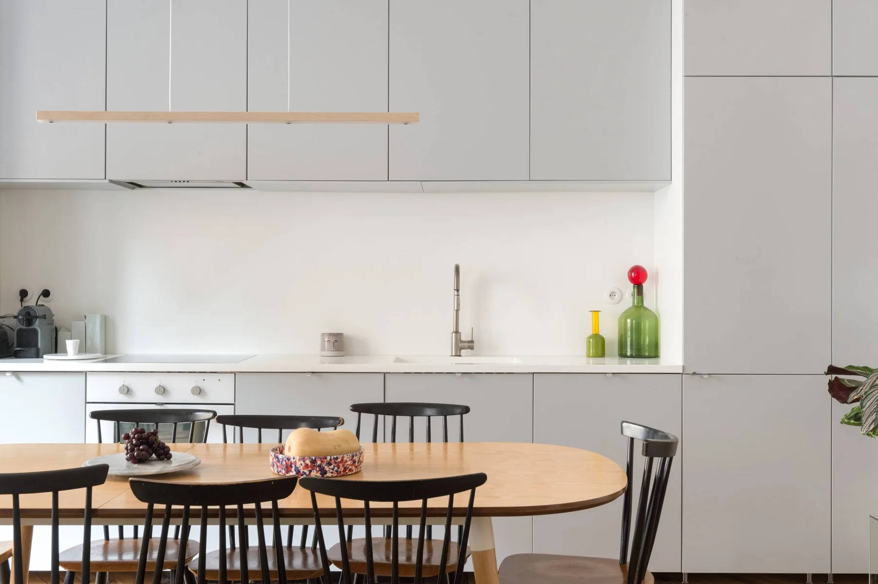 A dining table and seating stand in front of a bright, modern kitchen.
