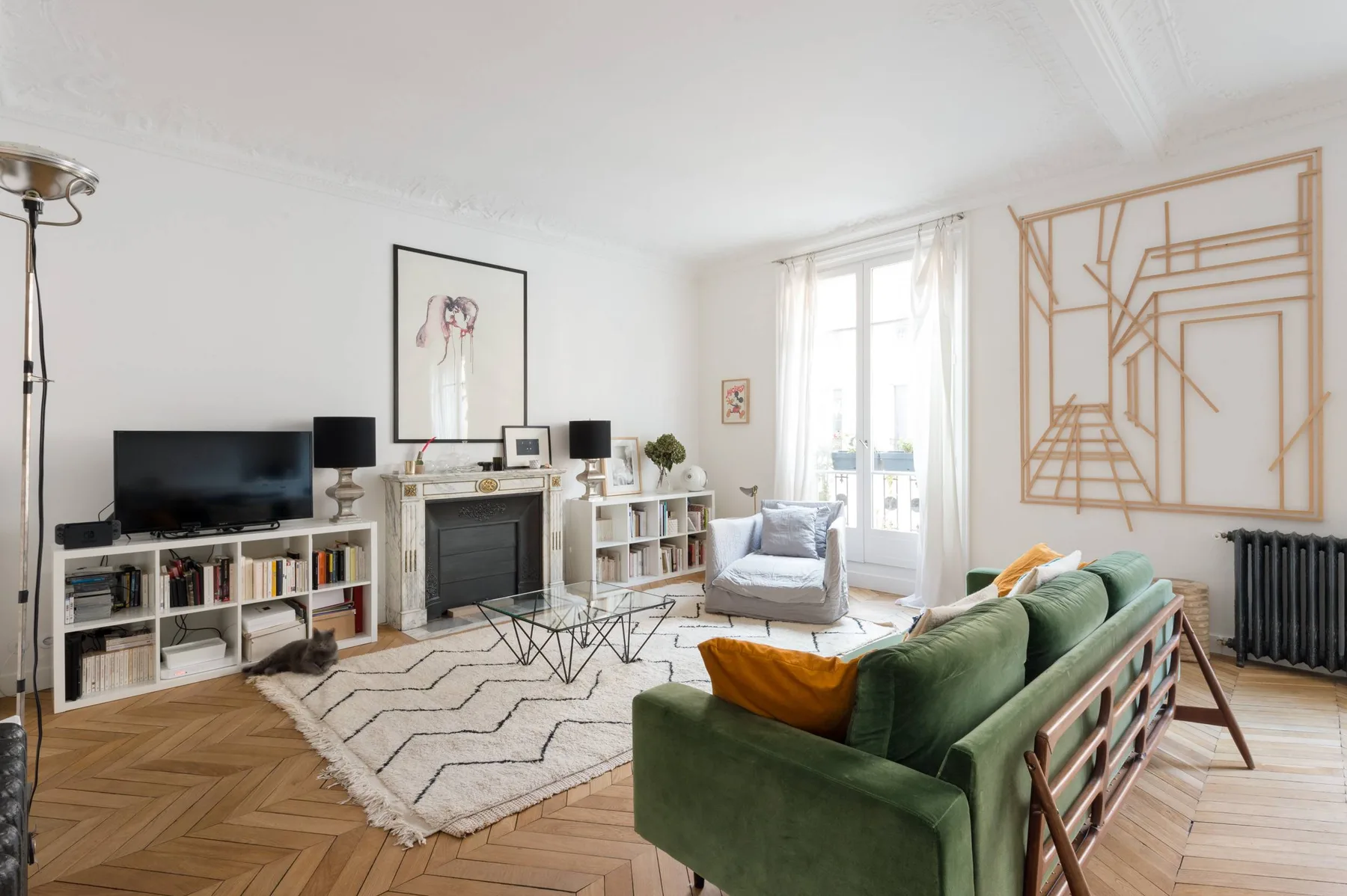 A bright living room with green seating, a fireplace, and large windows.