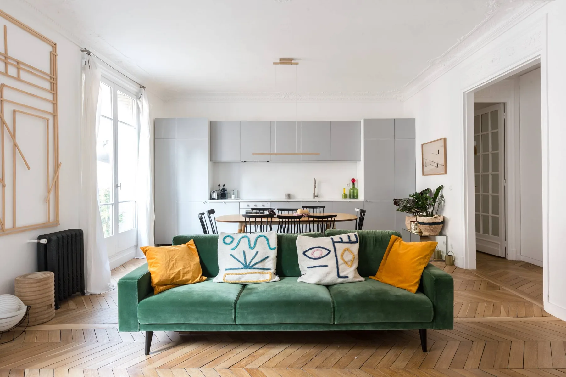 A bright living room with a green sofa facing an open kitchen.
