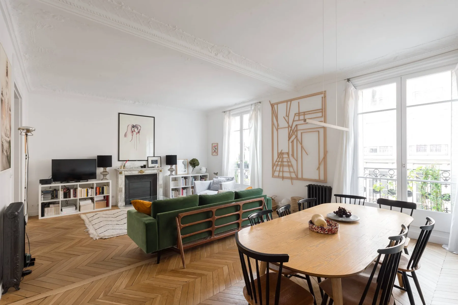 A bright living and dining room with a green sofa and a wooden dining table.