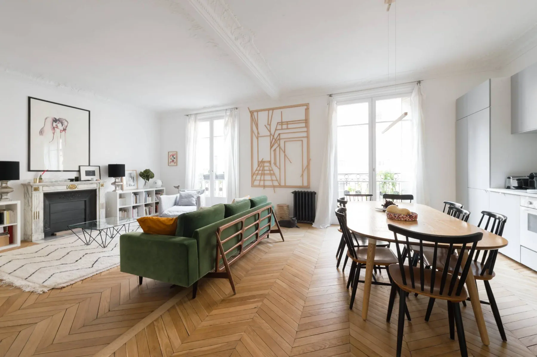 A bright living and dining room with green seating, a fireplace, and a wooden table.
