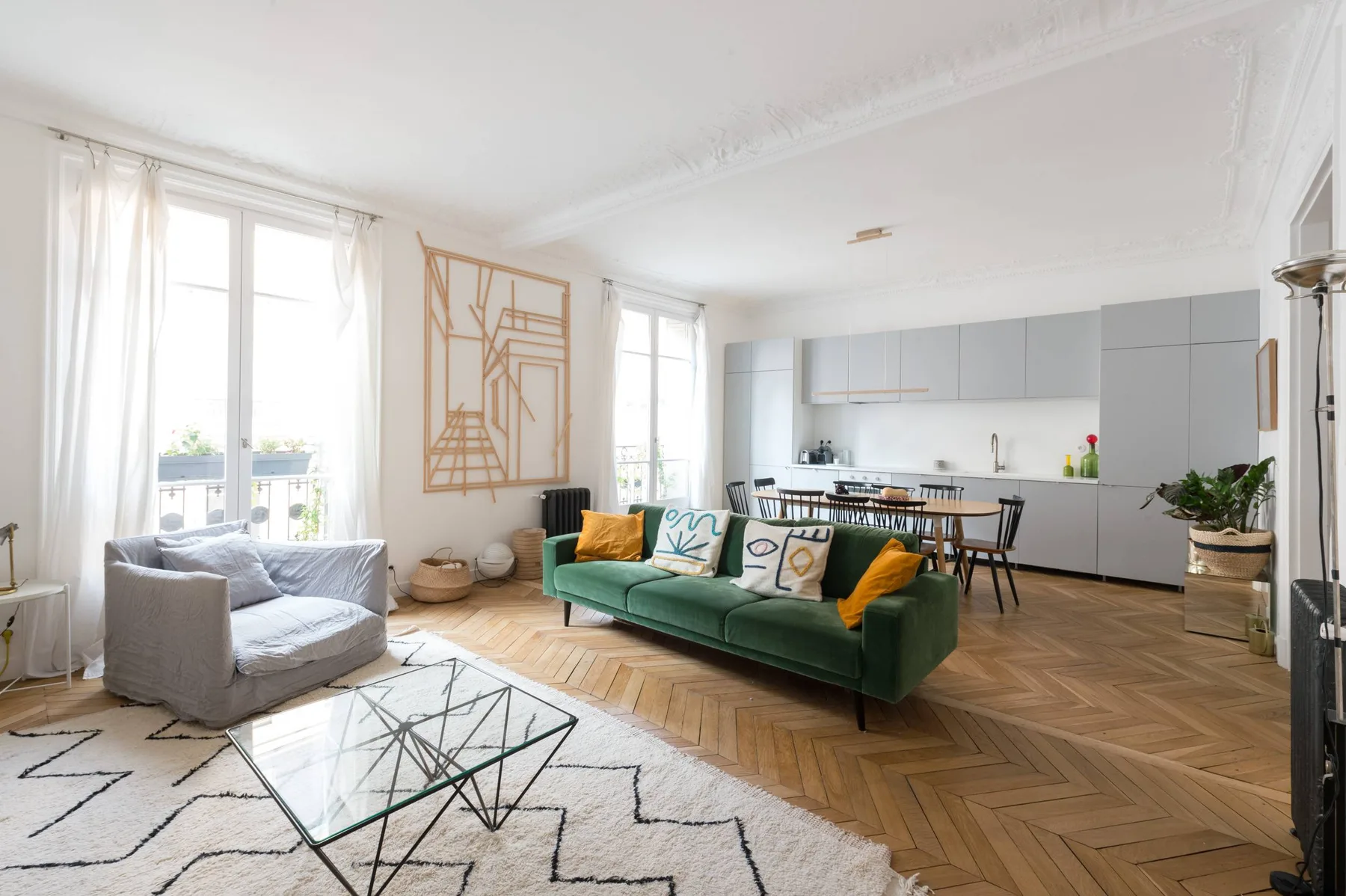 A bright living room with green seating beside an open kitchen and dining area.