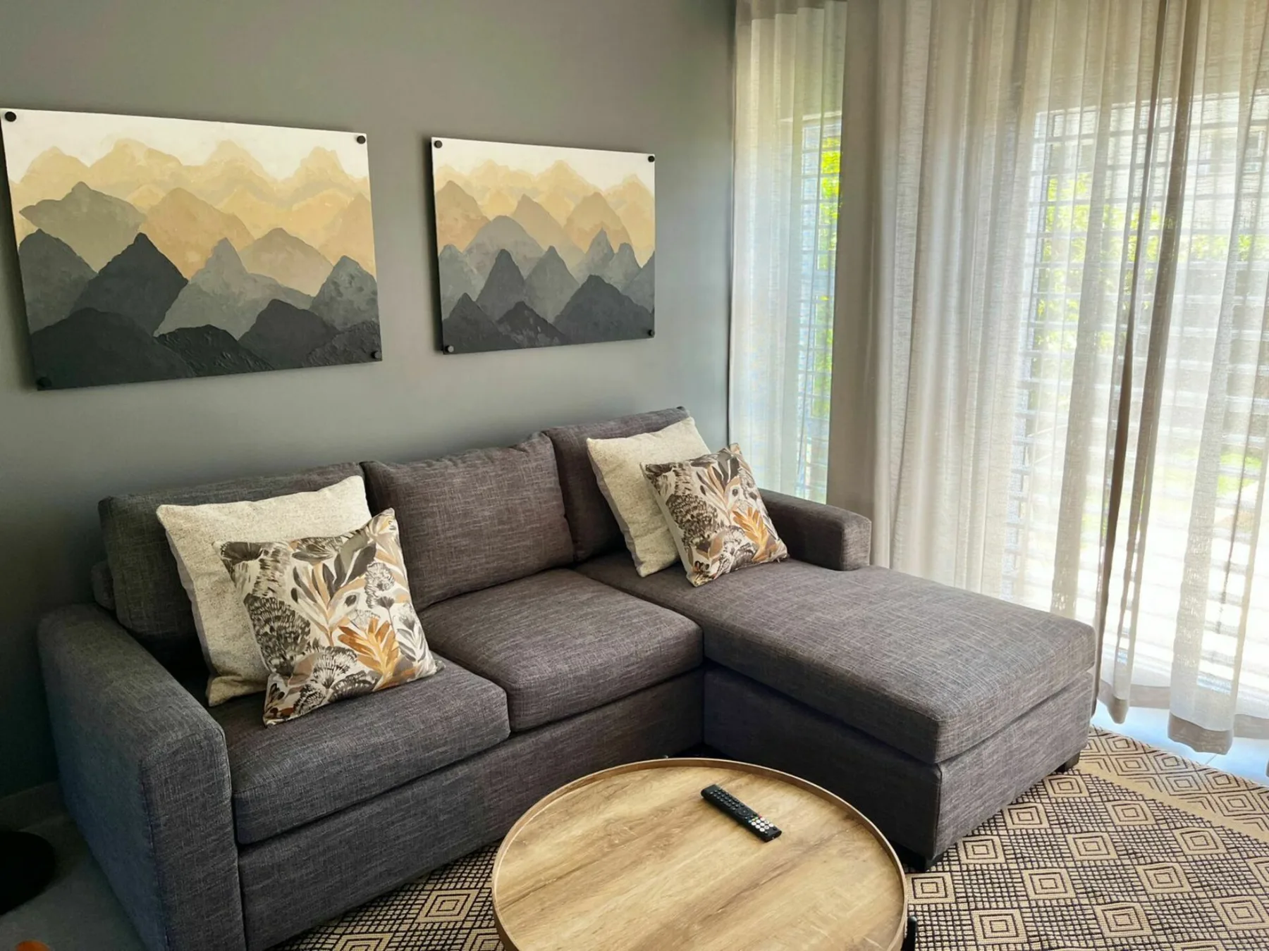 A living room with a gray sectional sofa and landscape artwork.