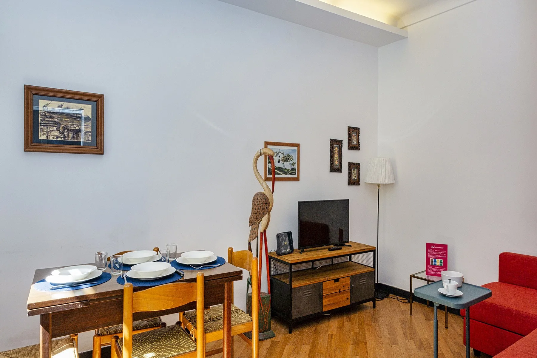 Zona de comedor y estar con una mesa de madera, un televisor y asientos rojos.