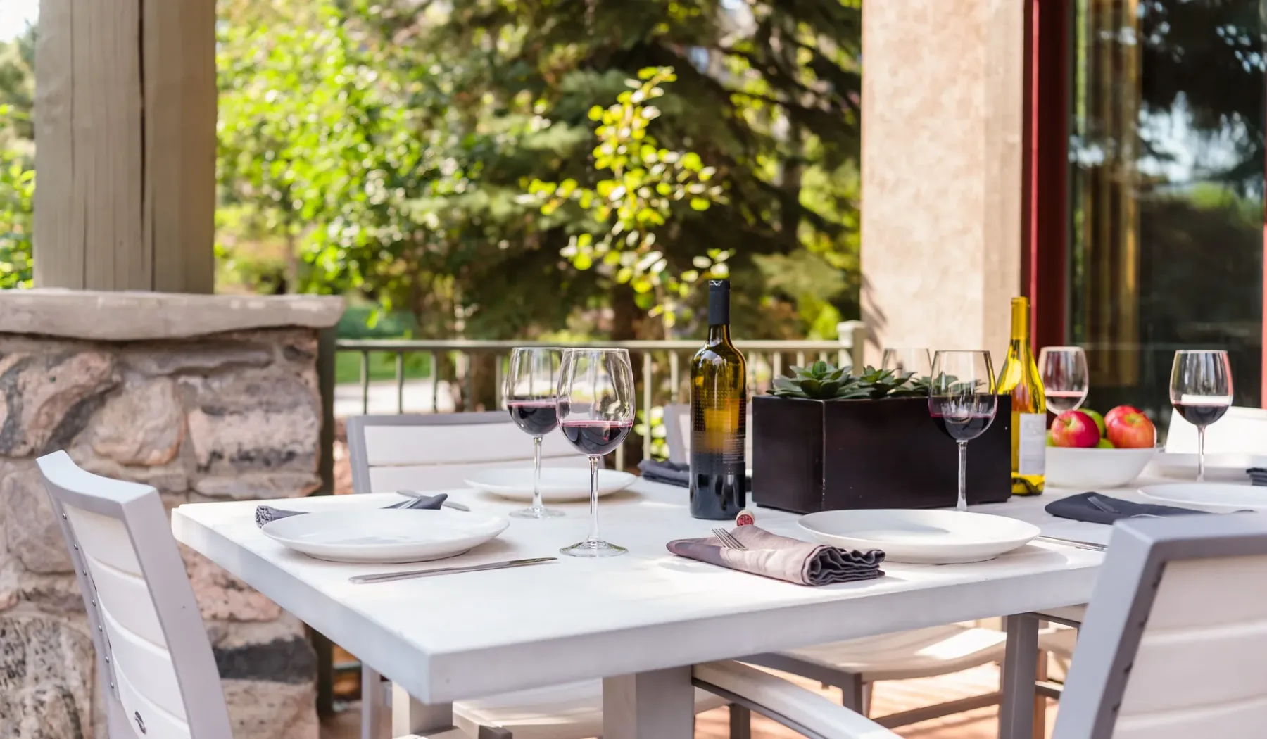 Una mesa de comedor al aire libre está preparada con platos, copas y botellas de vino.