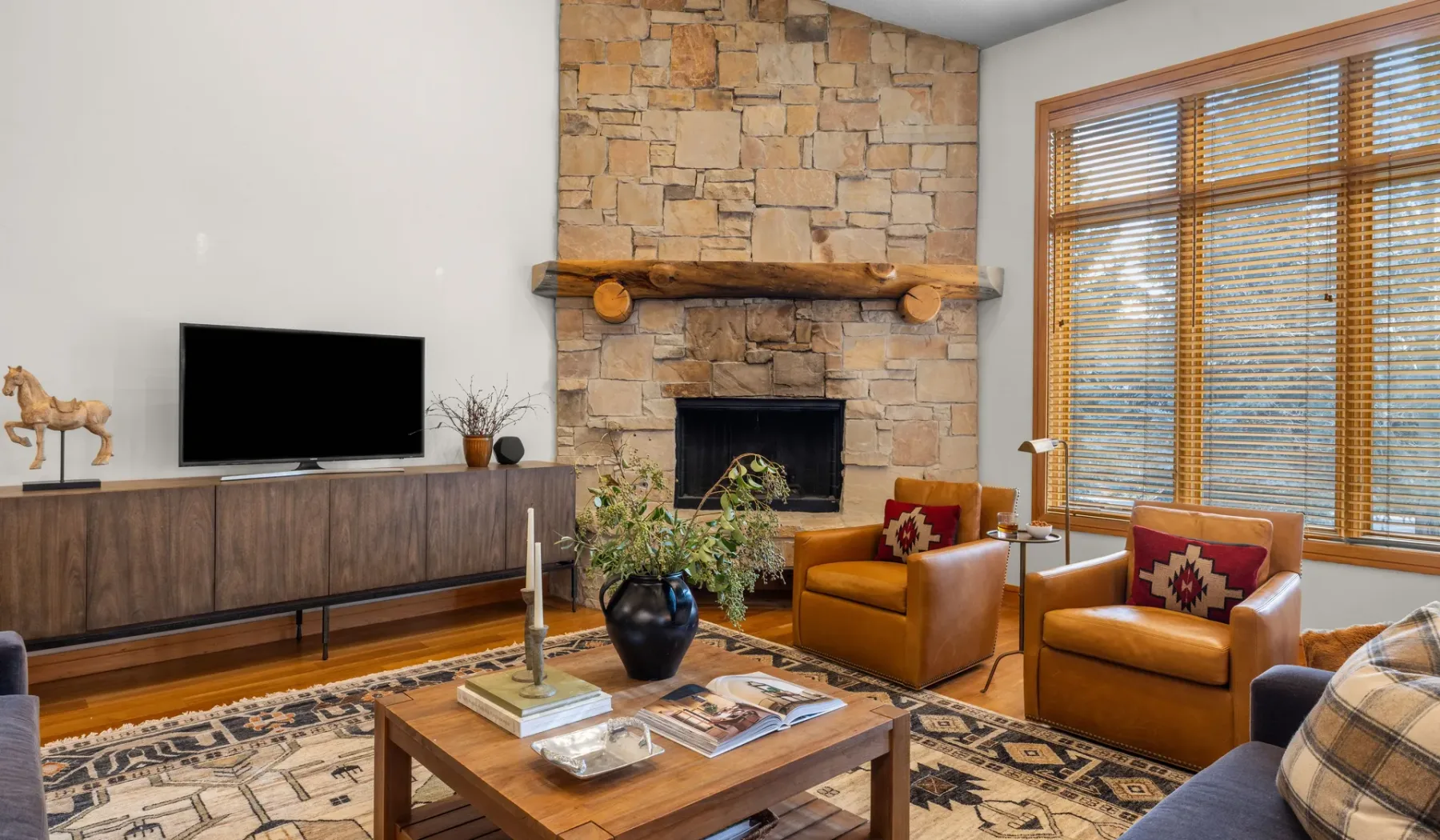 Una sala de estar con chimenea de piedra, asientos y ventanas grandes.