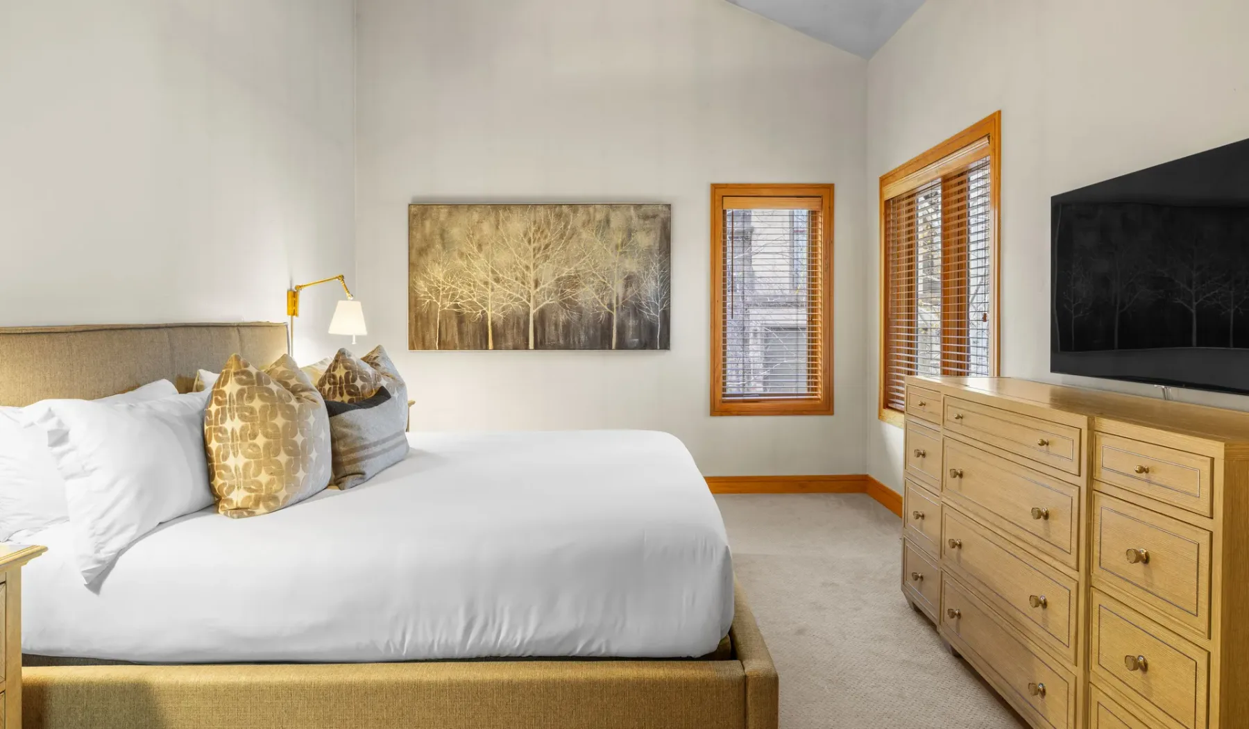 Dormitorio con una cama tendida, una obra enmarcada y una cómoda con un televisor.