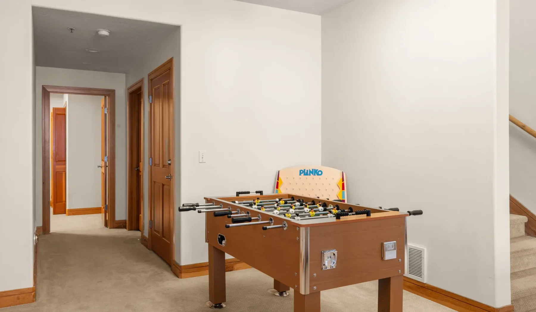 Una mesa de futbolín está en un pasillo junto a varias puertas de madera.
