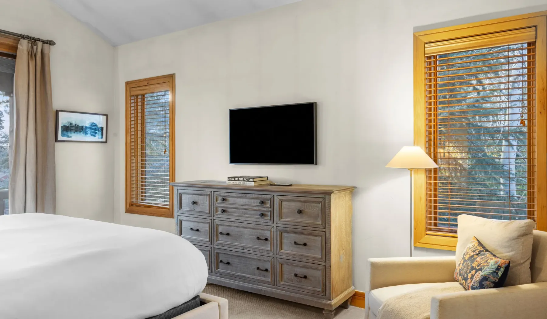 Un dormitorio con una cama, una cómoda y un televisor en la pared.