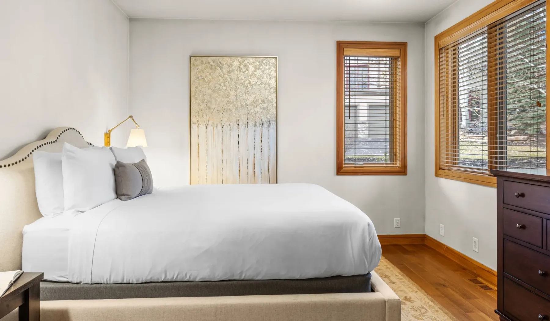Un dormitorio luminoso con una cama bien tendida y ventanas con persianas de madera.
