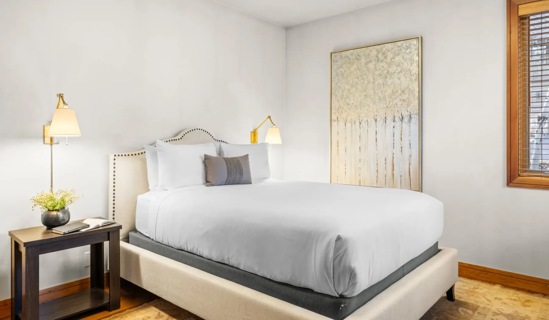Un dormitorio luminoso con una cama bien tendida y arte enmarcado en la pared.