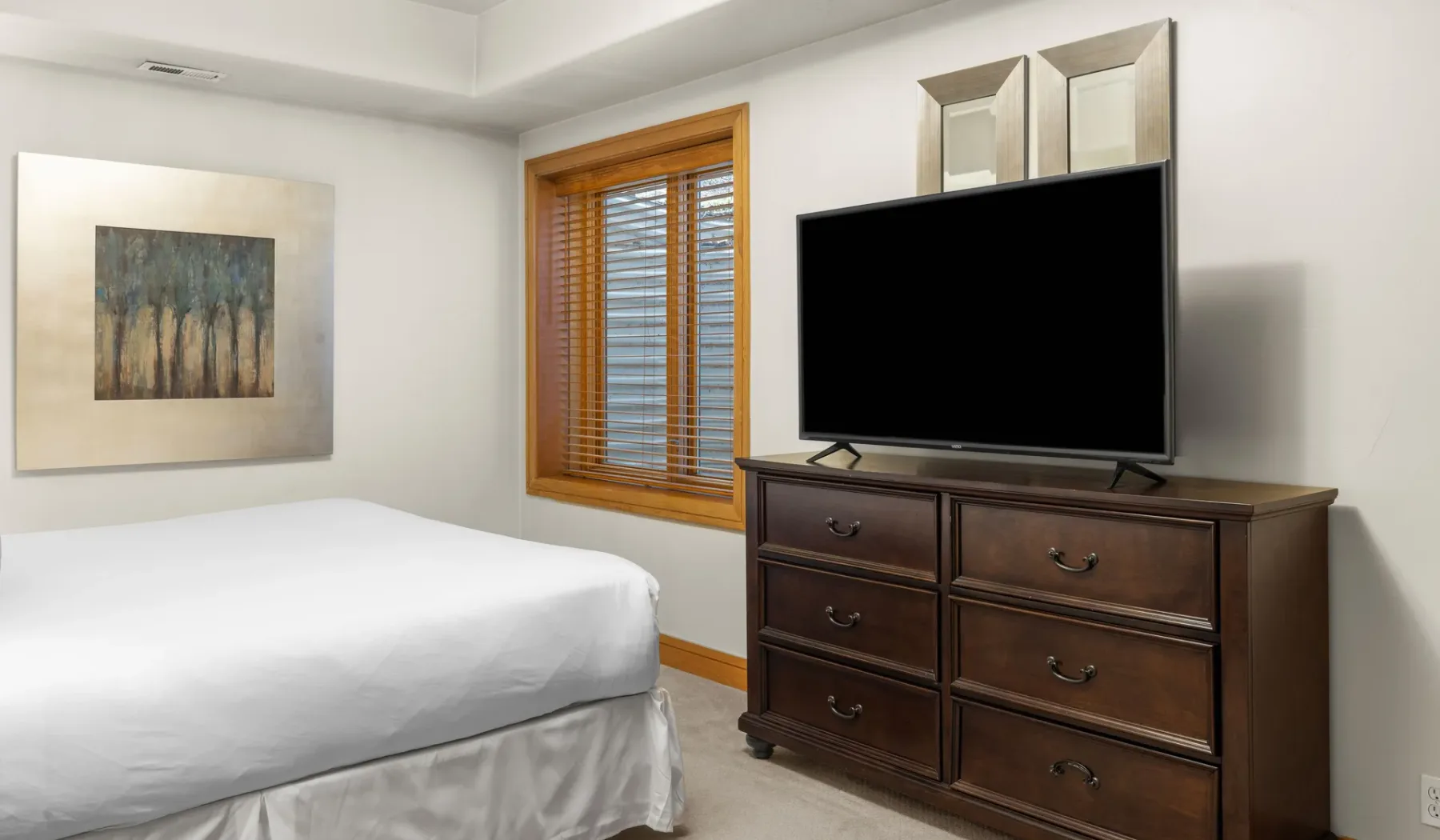Un dormitorio con una cama junto a una cómoda con un televisor encima.