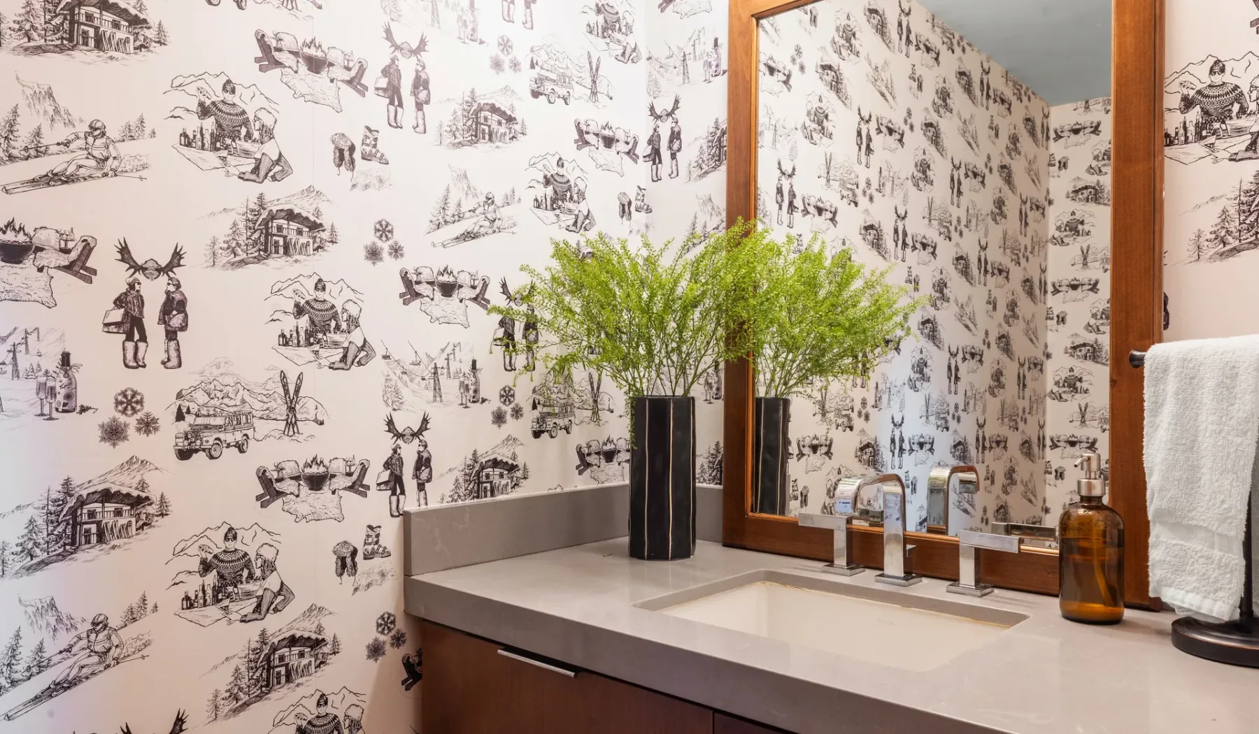Un tocador de baño con lavabo, espejo y papel tapiz estampado.