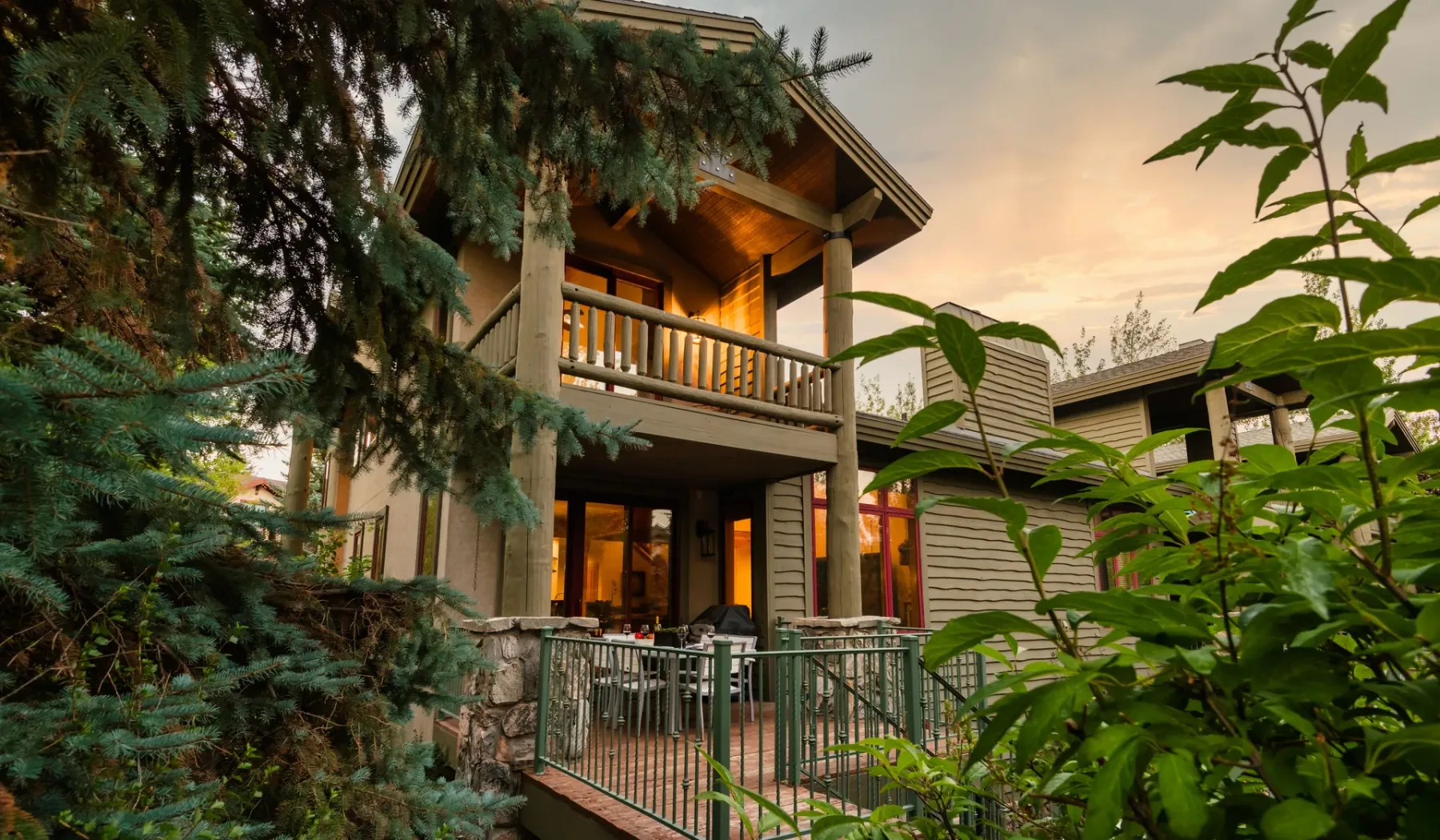 Una casa de madera con balcones y un patio cercado está entre árboles.