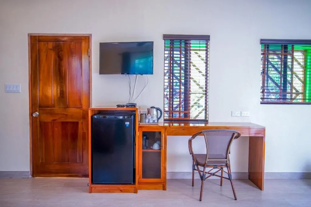 Interior de la suite con televisor, minirrefrigerador, escritorio y ventanas.