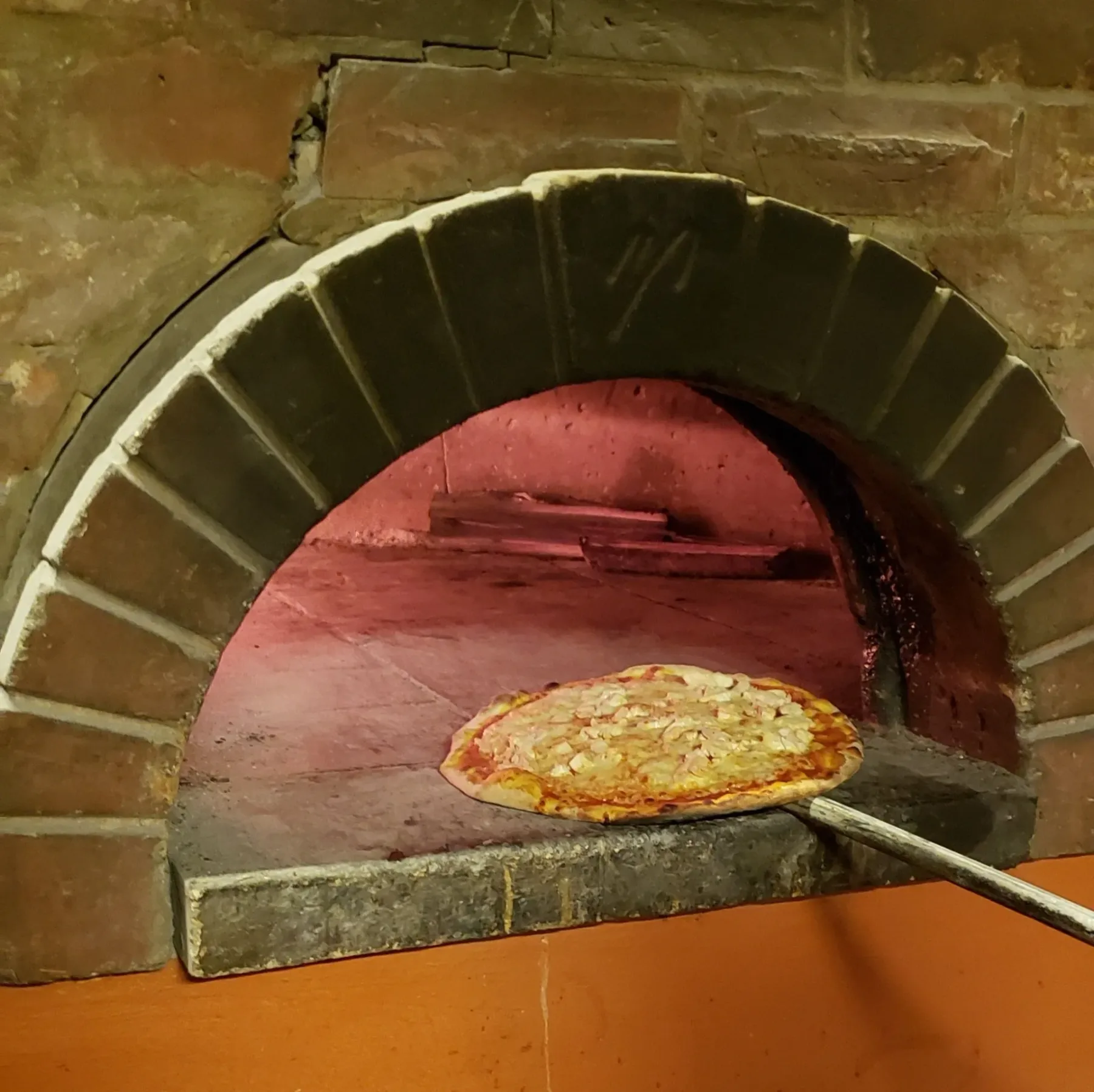 Pizza que se está sacando de un horno de ladrillo.