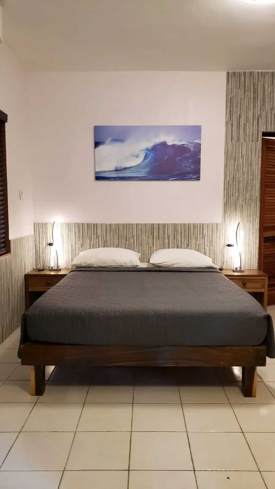 Habitación Ocean Mist con cama de madera, mesas de noche y una obra de arte con olas.