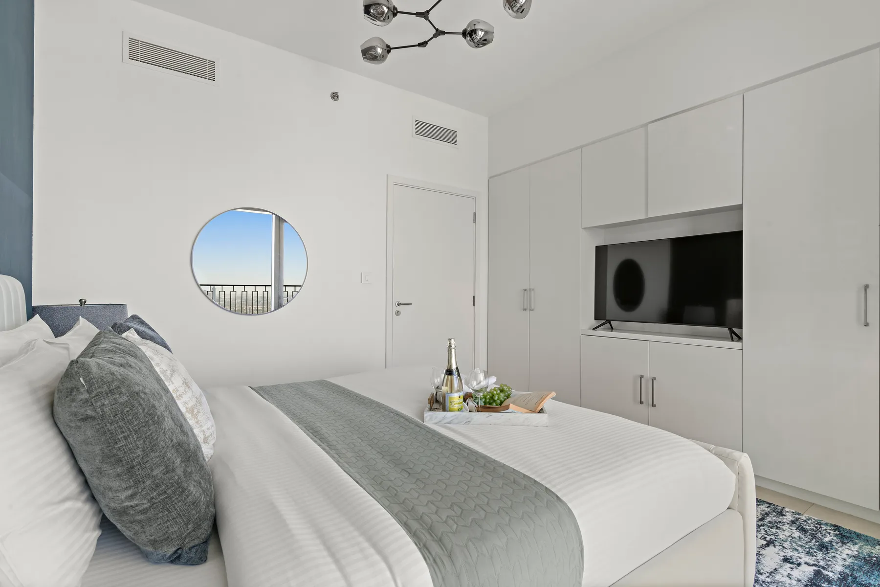 A bright bedroom with a neatly made bed and a television set into built-in cabinetry.