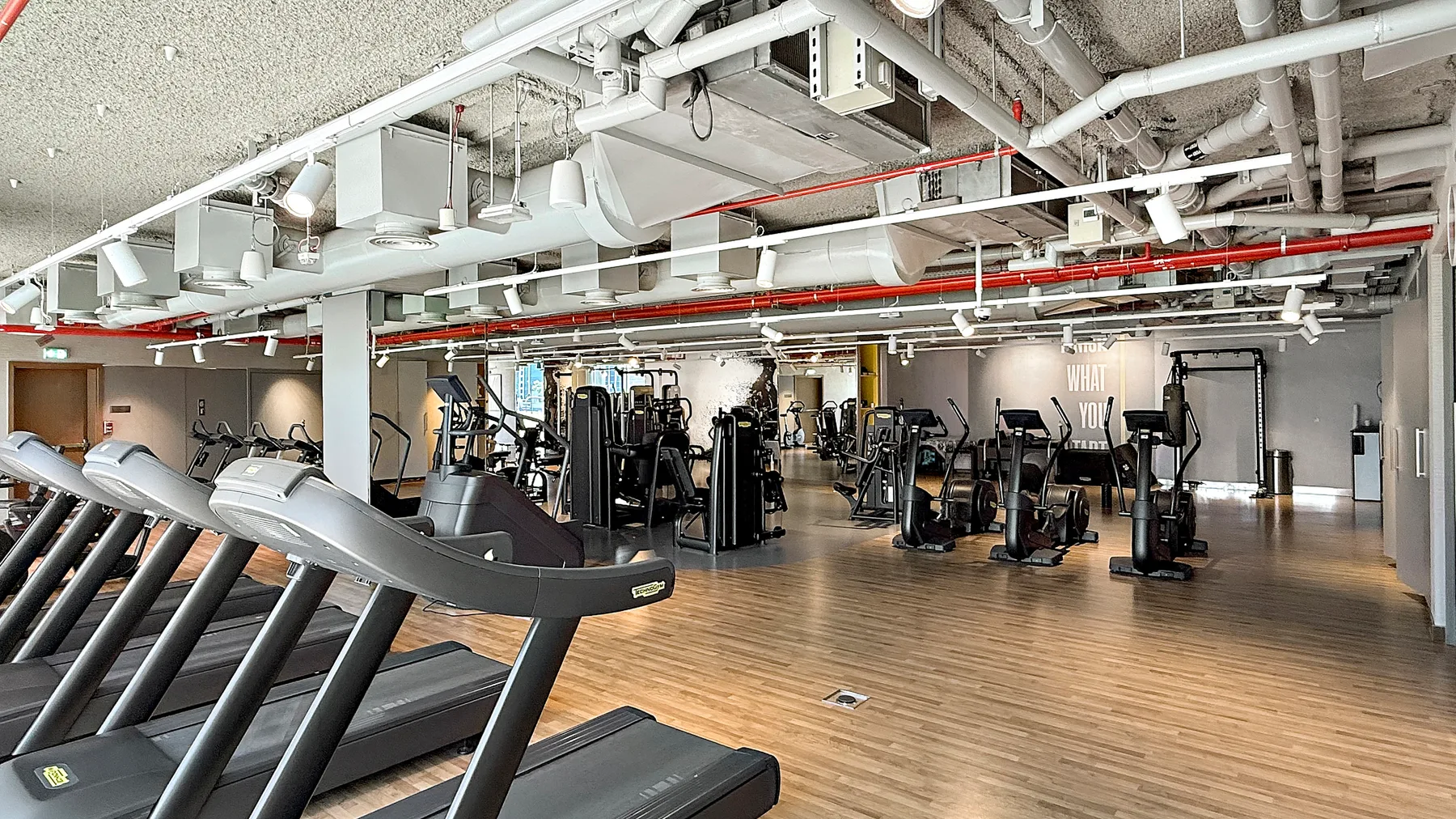 A gym with treadmills in the foreground and exercise equipment across the room.