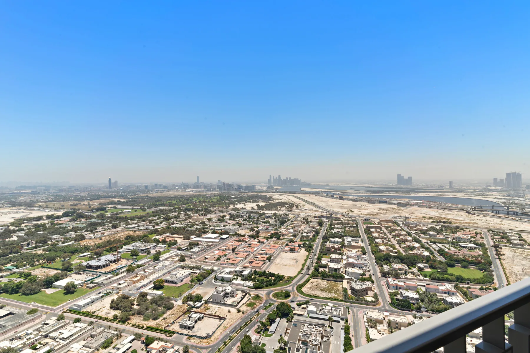 A broad cityscape with low-rise buildings, roads, and distant towers beneath a clear sky.