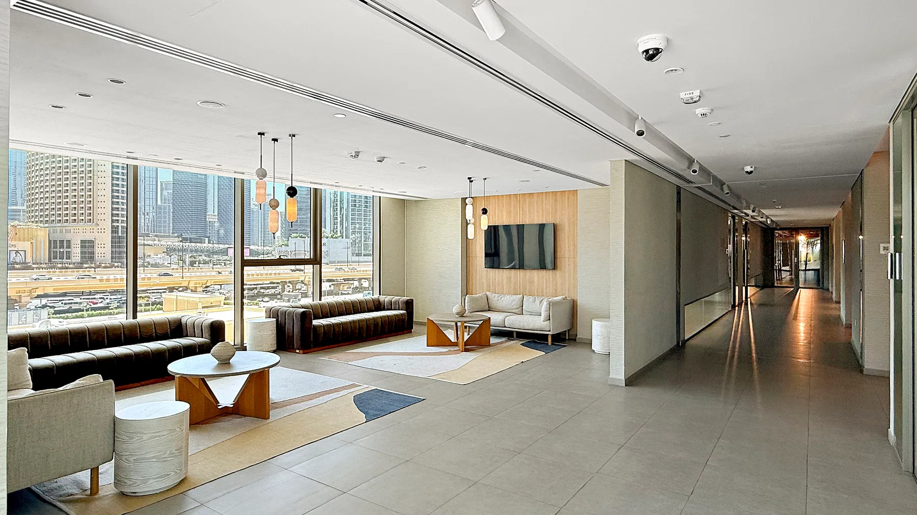 A modern lounge with seating, a low table, and large windows overlooking the city.