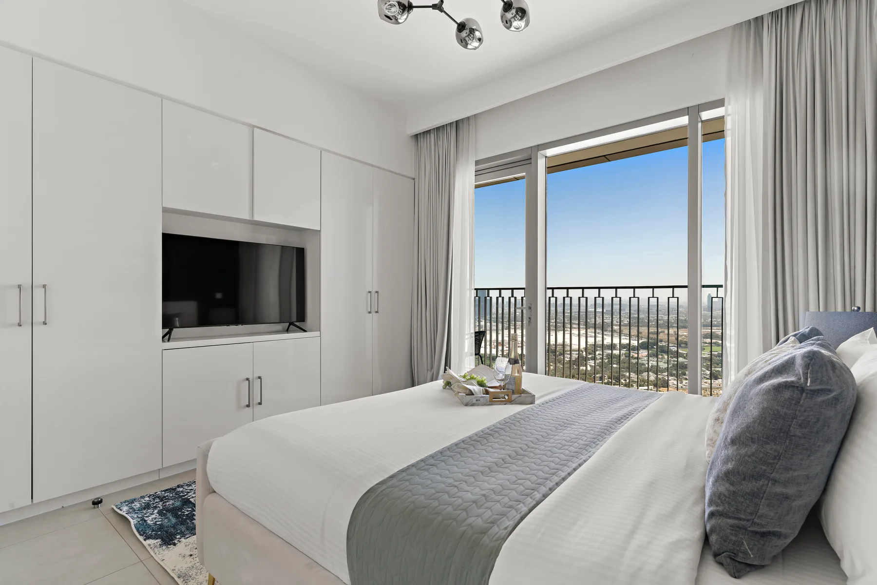 A bright bedroom with a bed facing large windows and a balcony railing.