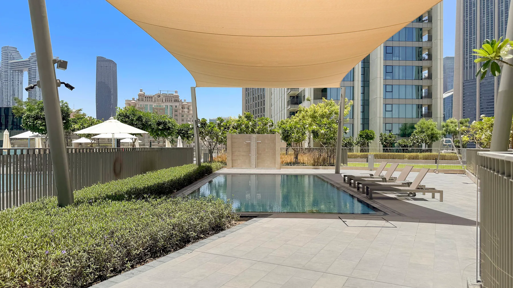 A rooftop pool sits beneath a shade canopy, with lounge seating and city buildings nearby.
