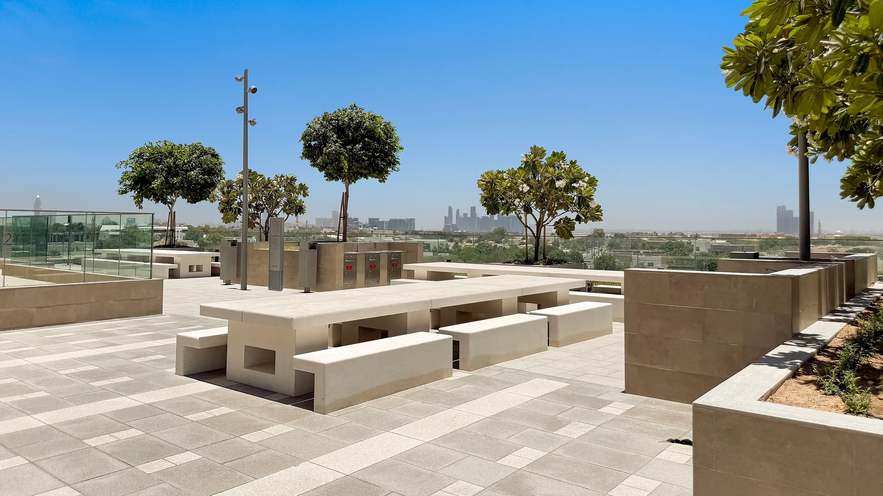 A sunlit outdoor terrace has built-in seating and planters beneath a clear blue sky.