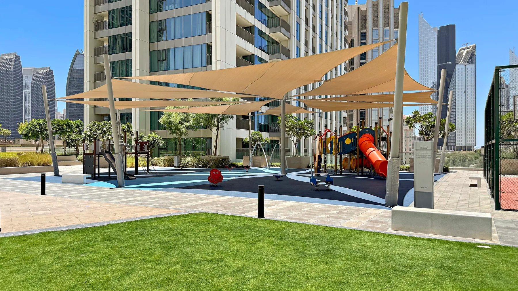 An outdoor playground with colorful play equipment beneath large shade sails.