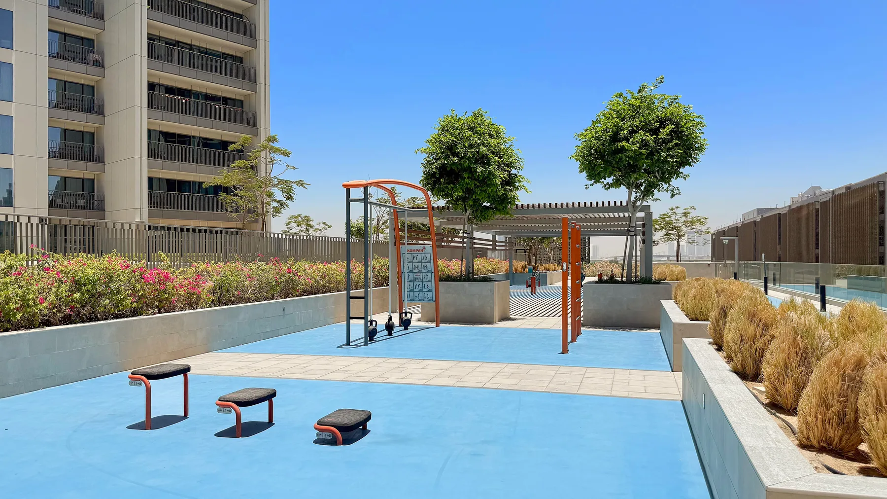 An outdoor exercise area with fitness equipment and planted beds.