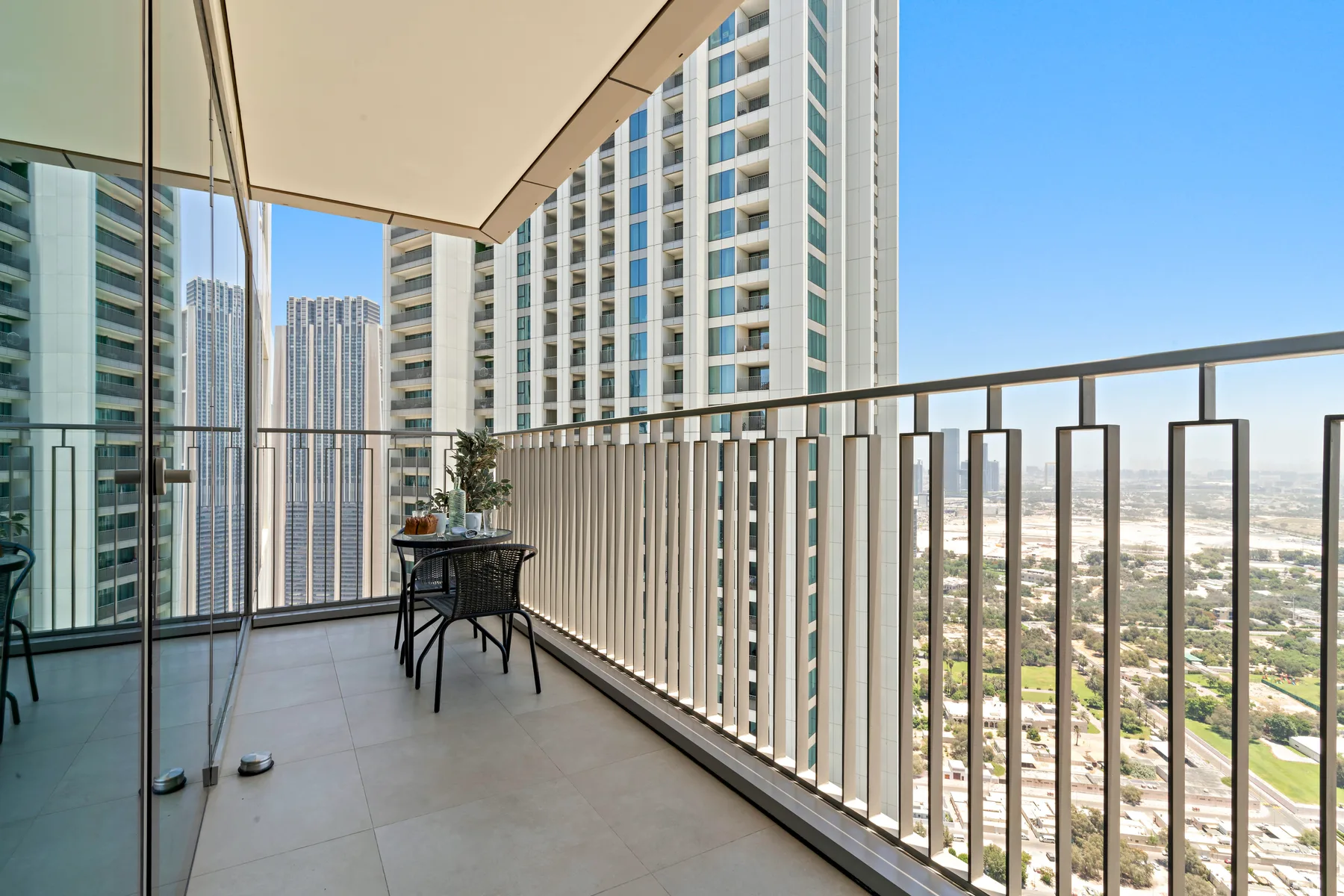 A balcony with outdoor seating overlooks nearby high-rise buildings and the city.