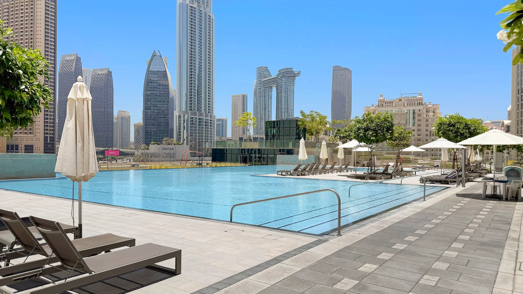 A rooftop swimming pool with lounge seating and a city skyline beyond.