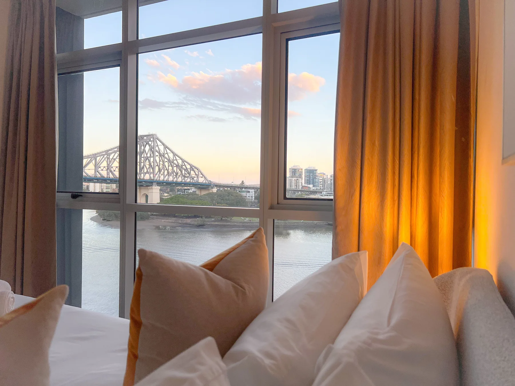 Un dormitorio con una cama junto a grandes ventanales con vistas a un río y un puente.