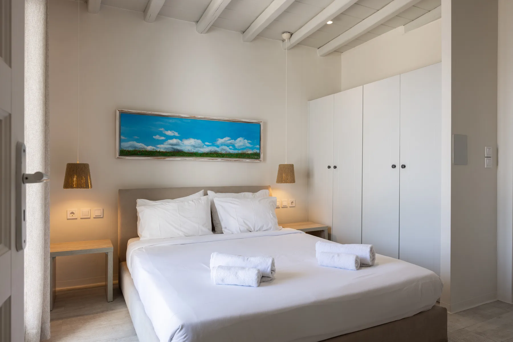 A bedroom with a neatly made bed, bedside tables, and a framed landscape picture.