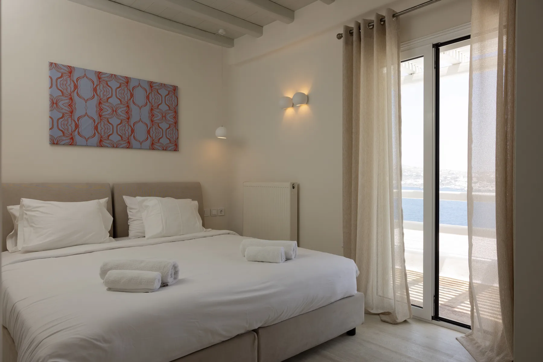 A bedroom with a neatly made bed and glass doors opening onto a balcony.