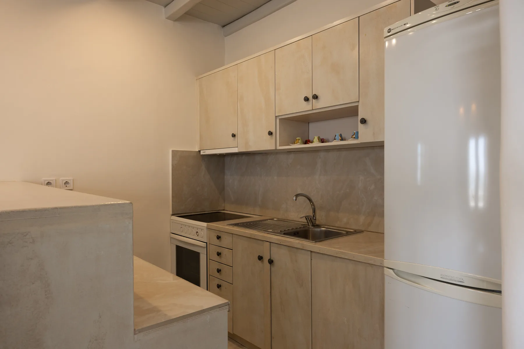 A compact kitchen with light wood cabinets, a countertop, and a refrigerator.