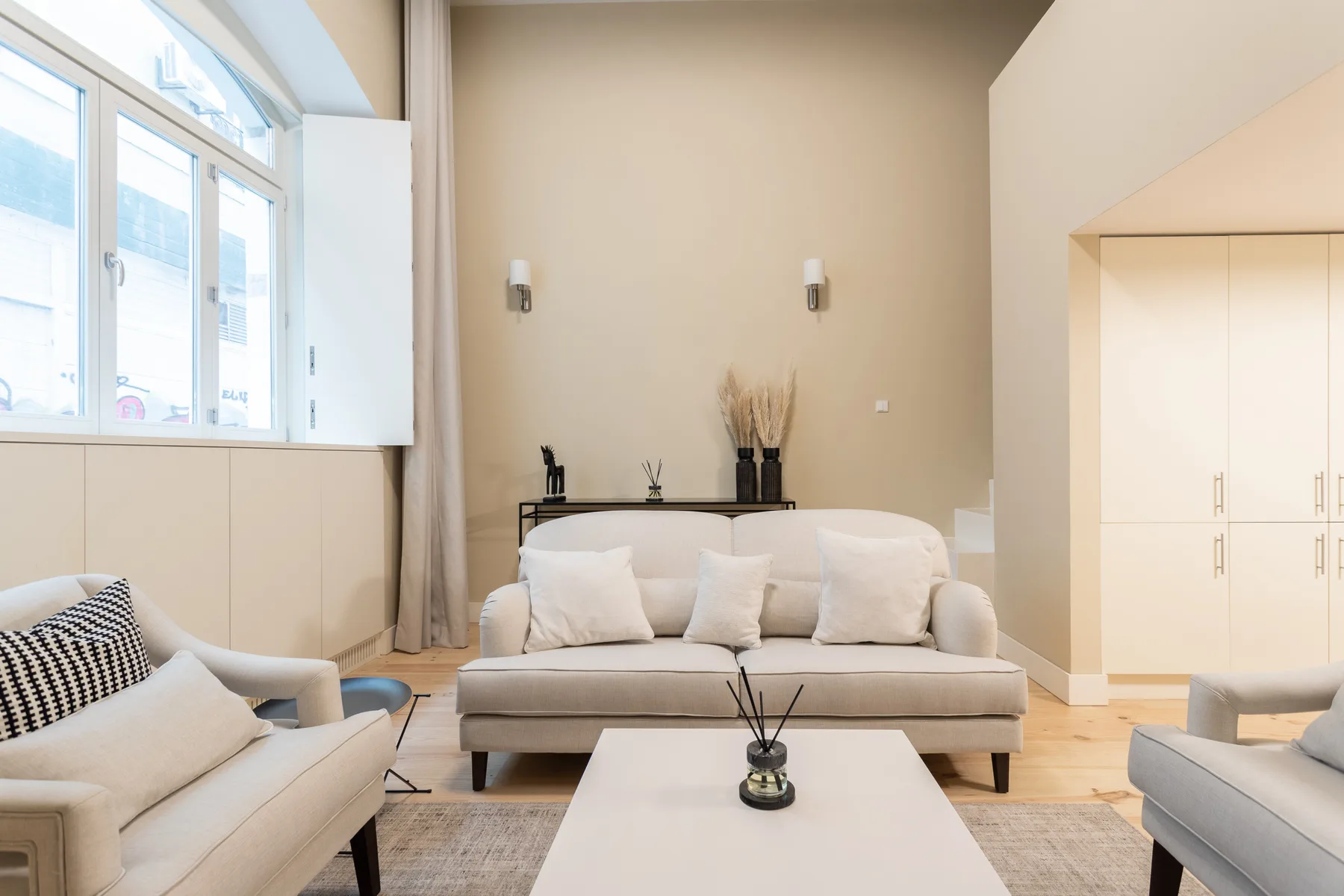 A bright living room with a central sofa and large windows.