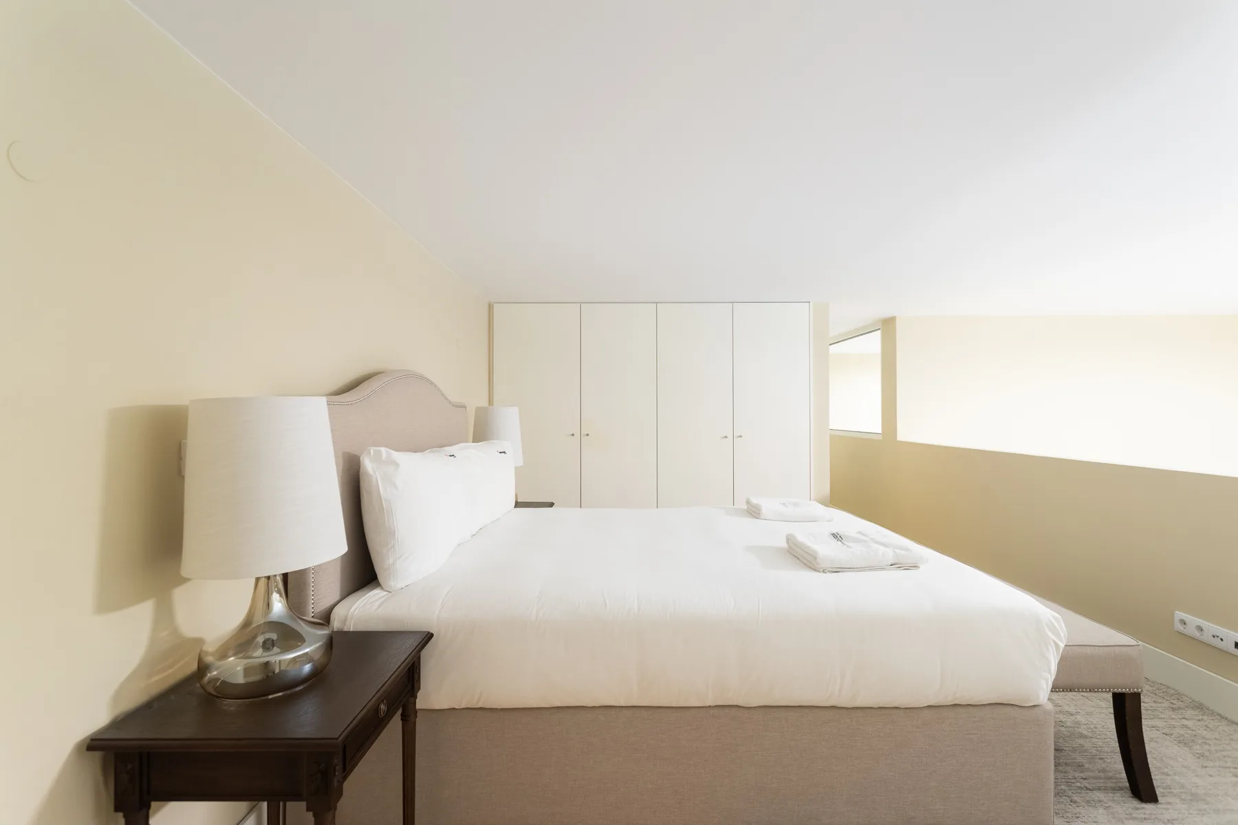 A bright bedroom with a neatly made bed and white wardrobes.