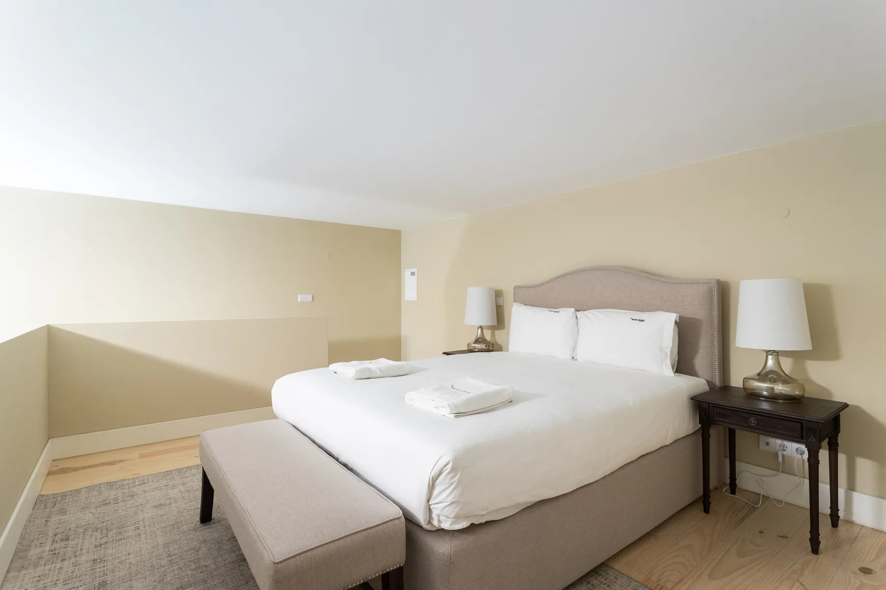 A bedroom with a neatly made bed and a cushioned bench at its foot.
