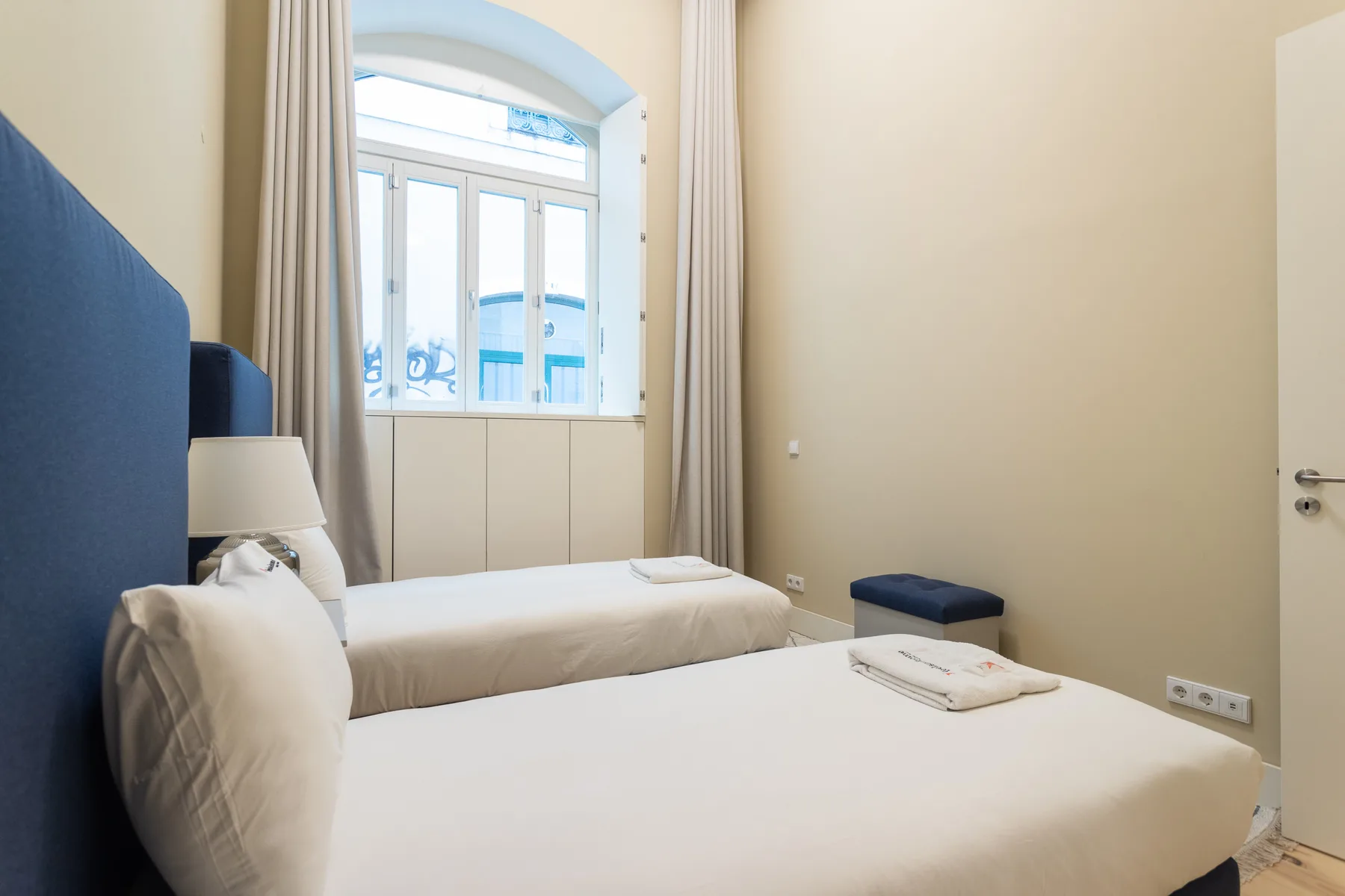 A bedroom with two beds and a large arched window.