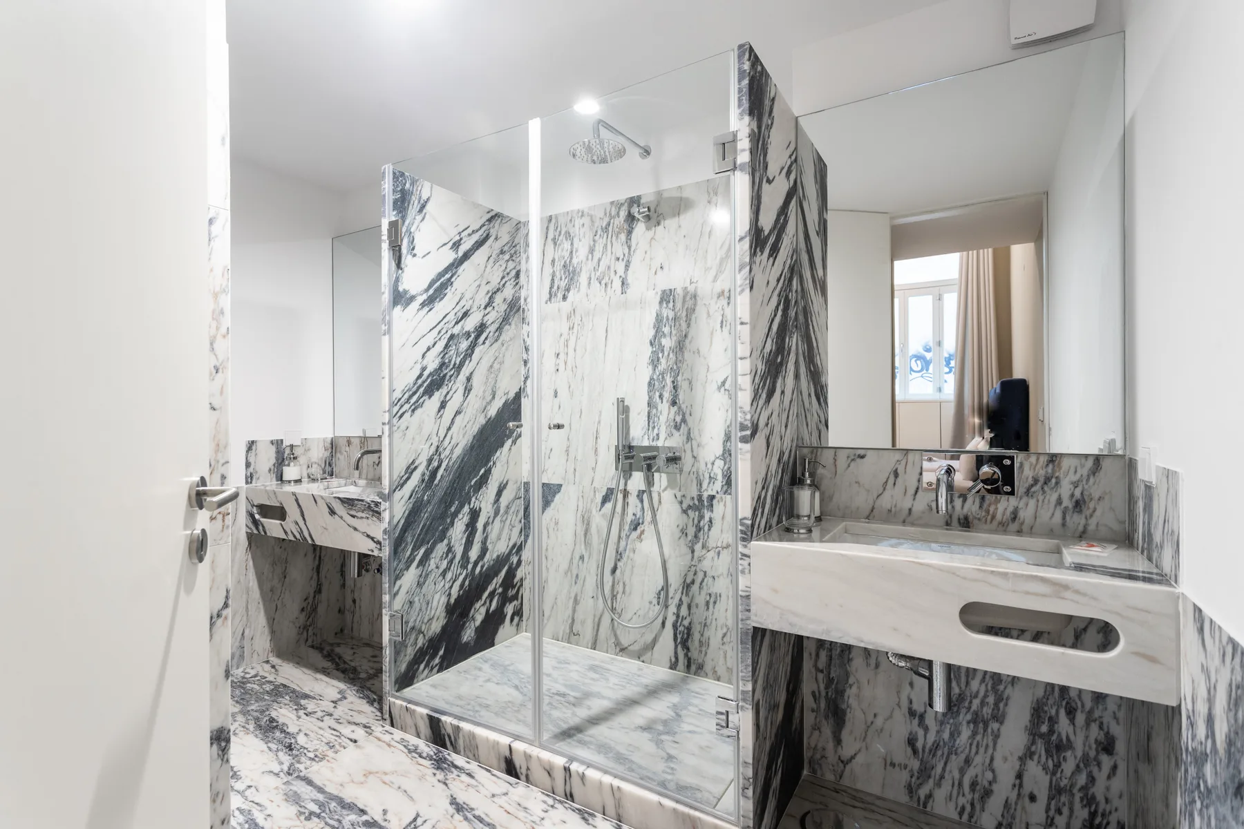 A bright bathroom with a glass shower and a long marble vanity.