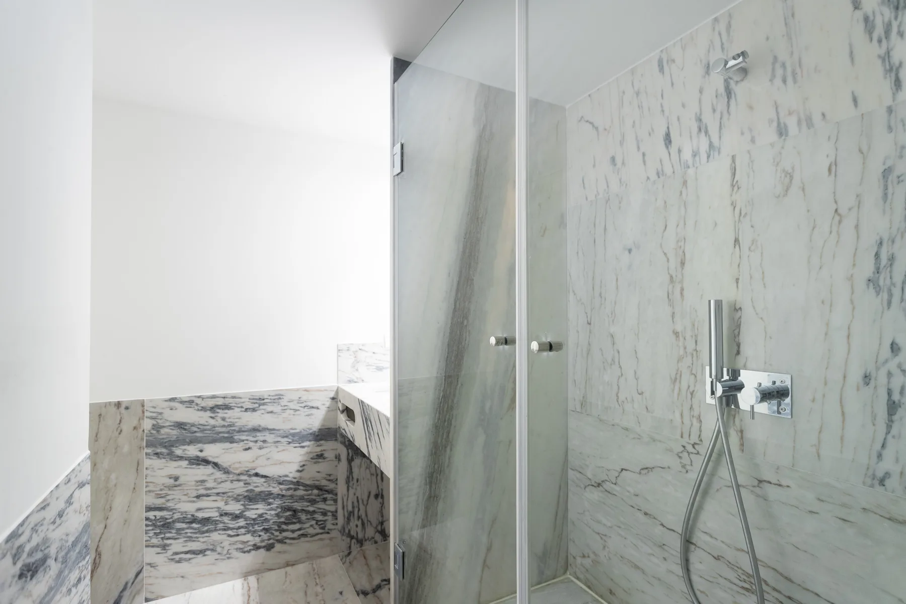 A marble bathroom with a glass shower and pale stone walls.