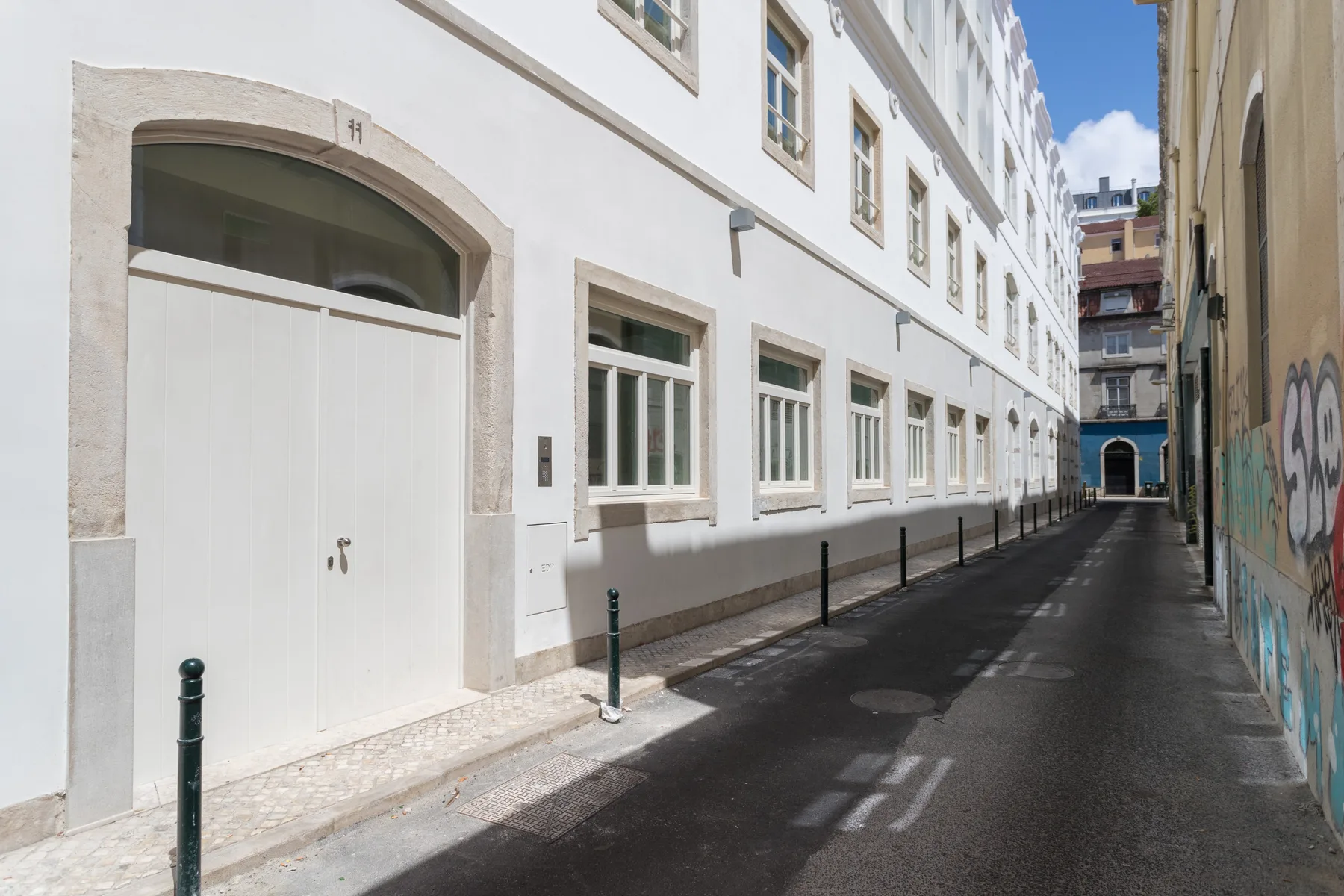 A narrow street runs between a white building and a wall covered in graffiti.