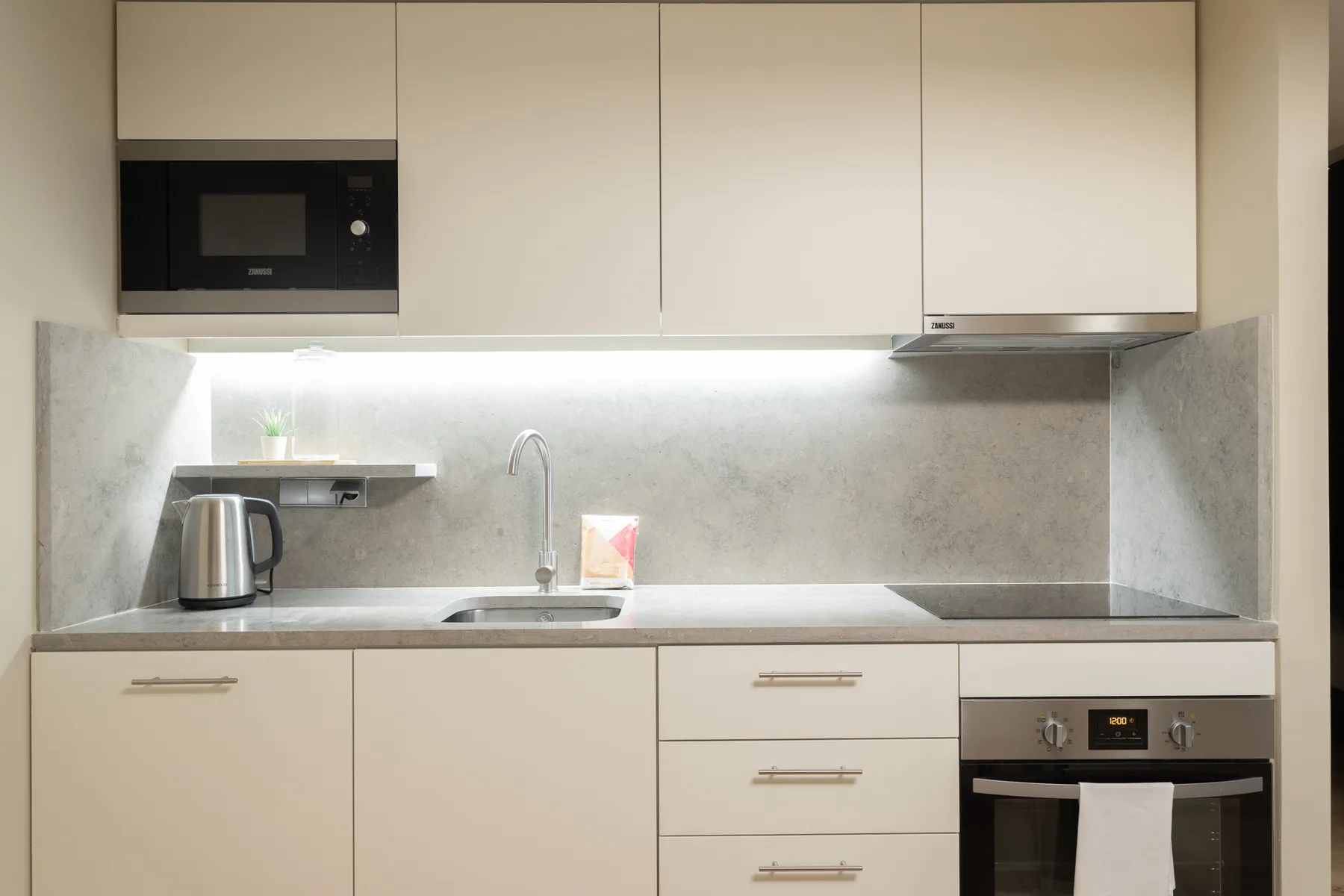 A modern kitchen with pale cabinets, a sink, and built-in appliances.