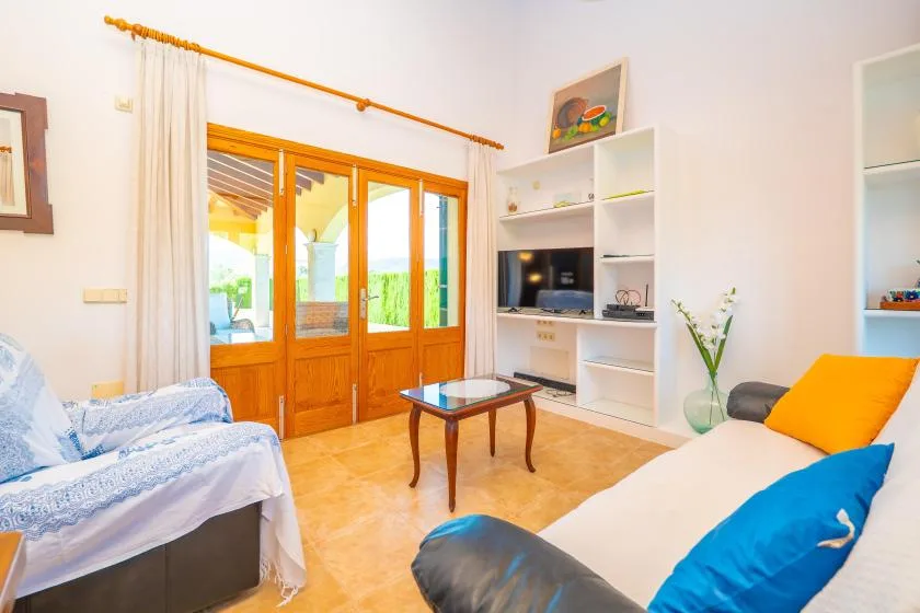 A bright living room with seating, a television, and glass doors opening onto greenery.