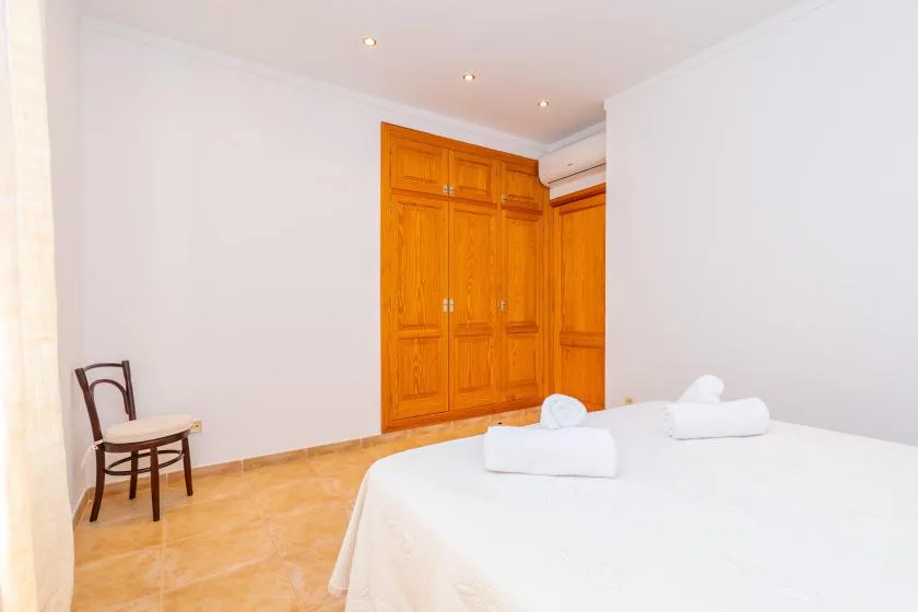 A bedroom with a bed, wooden wardrobe, and chair.